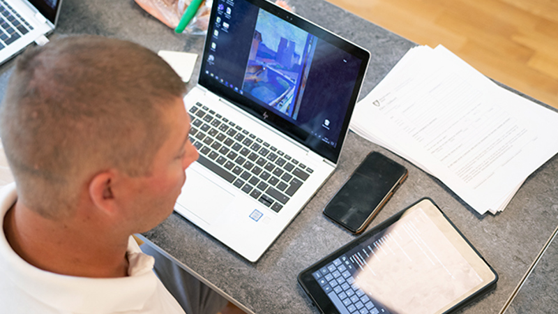 En man med papper, en dator, en mobiltelefon och en Ipad framför sig på bordet.