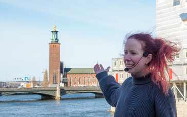 En person med headset pratar och pekar på Stockholms stadshus.