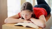 En flicka ligger på mage och läser en bok.