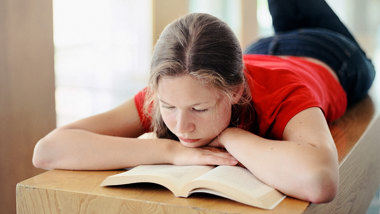 En flicka ligger på mage och läser en bok.