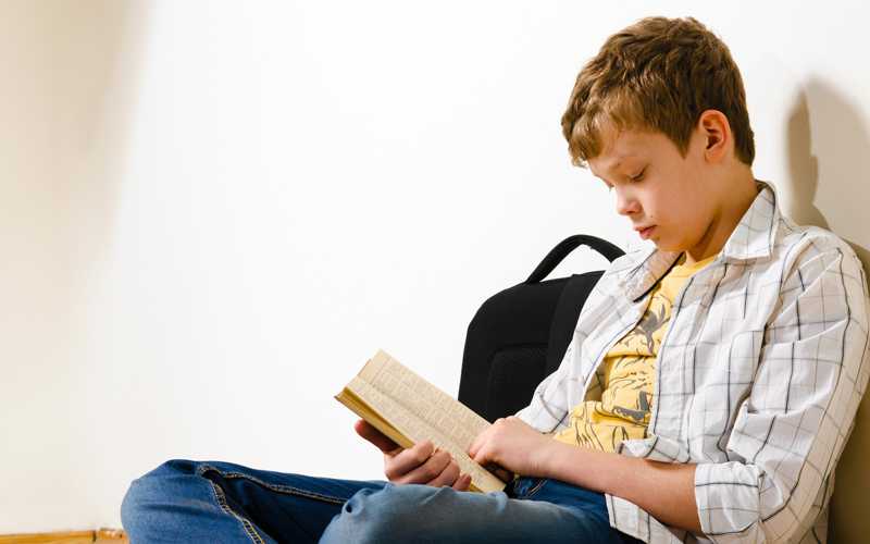En pojke sitter på golvet med ryggen mot en vägg och läser