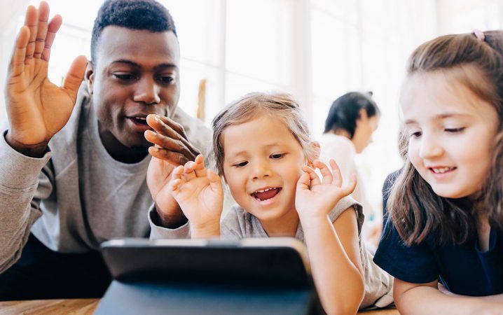 Förskollärare tittar på en surfplatta tillsammans med två flickor.