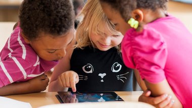 Tre barn tittar på en surfplatta.