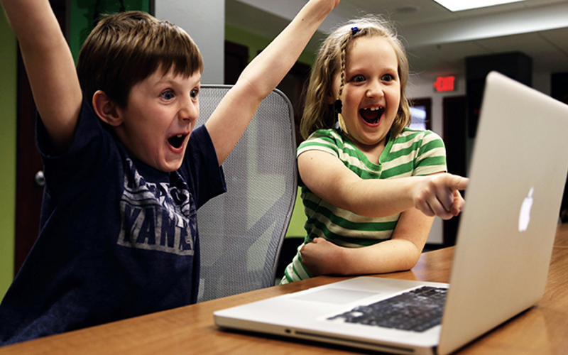 En pojke och en flicka tittar på film på en dator.
