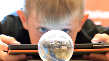 En elev programmerar en robot som ser ut som en boll med en ipad.