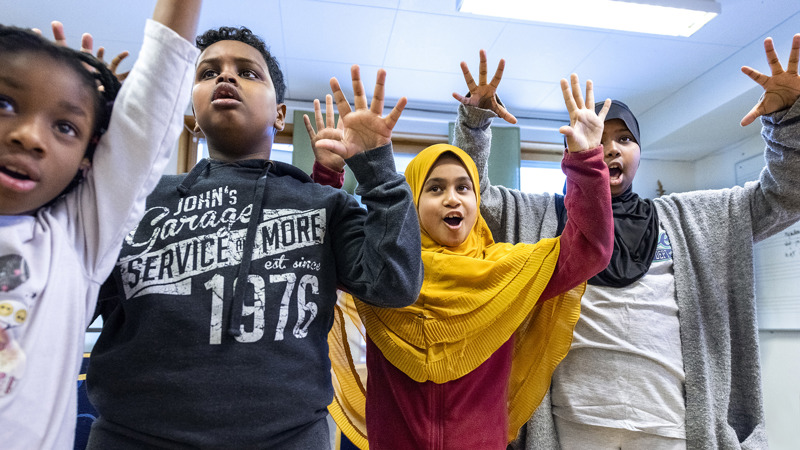 Fyra elever håller upp händerna i luften.