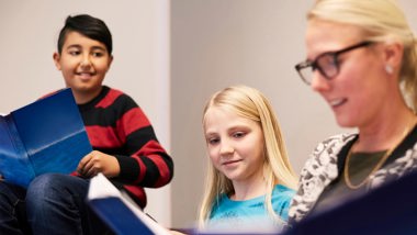 Två elever i högstadiet och en lärare läser ur var sin bok som de har i händerna.