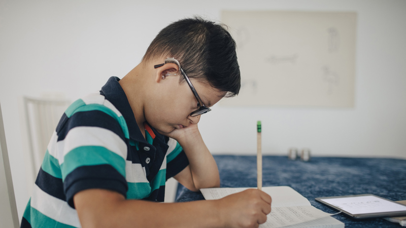 Pojke håller huvudet i handen, skriver i en skrivbok.
