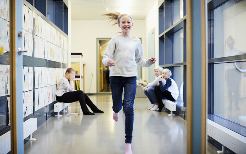 Leende flicka springer i skolans korridor