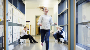 Leende flicka springer i skolans korridor