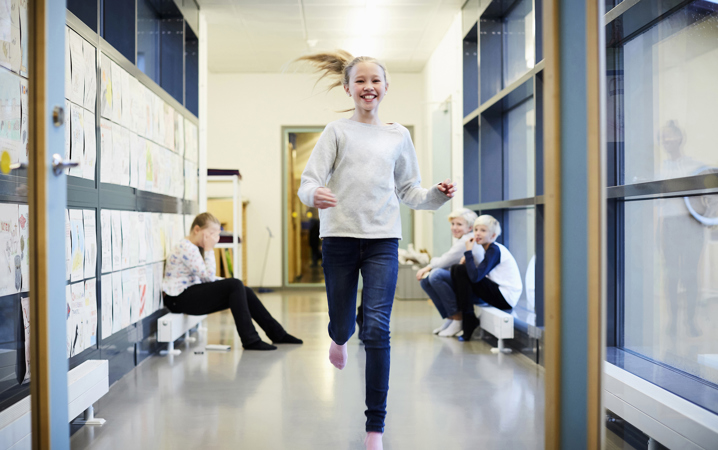Leende flicka springer i skolans korridor