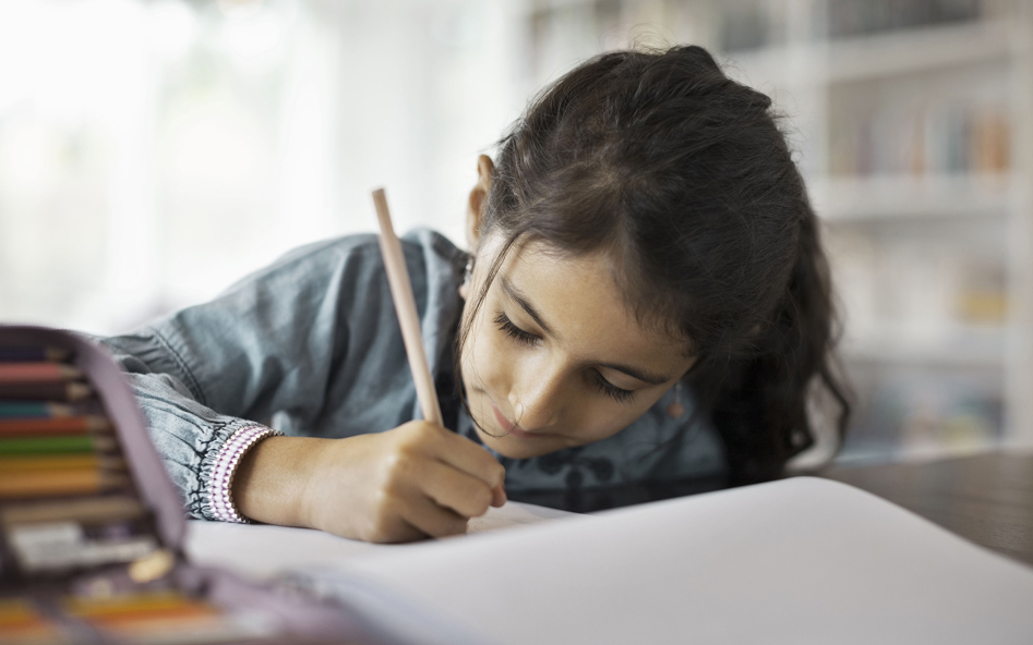 Flicka sitter vid ett bord och skriver med penna i ett block.