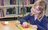 En flicka i ett biblioteket har handen på en bild i en bok. 