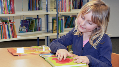 En flicka i ett biblioteket har handen på en bild i en bok. 