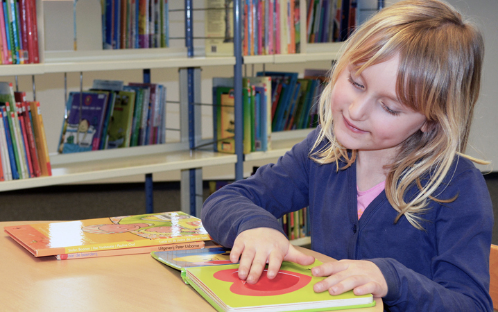 En flicka i ett biblioteket har handen på en bild i en bok. 