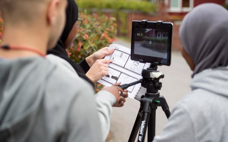 Elever spelar in film med en surfplatta på ett stativ.
