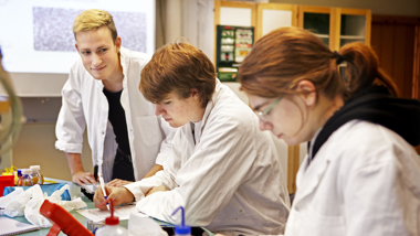 Tre ungdomar klädda i skyddskläder i kemilabb.