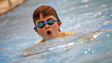 Pojke i högstadieålderns med simglasögon simmar intensivt i en bassäng.