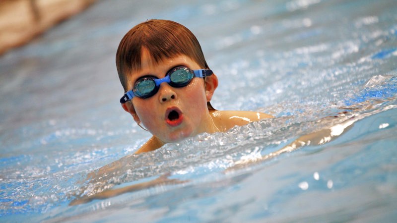 Pojke i högstadieålderns med simglasögon simmar intensivt i en bassäng.