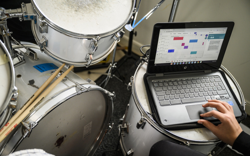 En hand fingrar på en laptop som är placerad ovanpå en stor trumma, som del av ett större trumset.