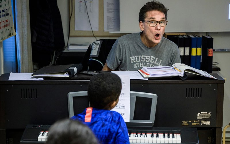 En lärare sjunger framför elever som sitter vid var sitt piano.