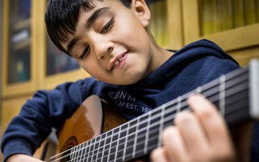 En pojke spelar gitarr med stor koncentration.