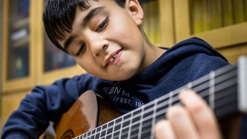 En pojke spelar gitarr med stor koncentration.