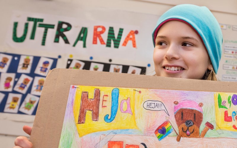 En elev håller upp en teckning med ordet heja och en seriefigur som säger heja.