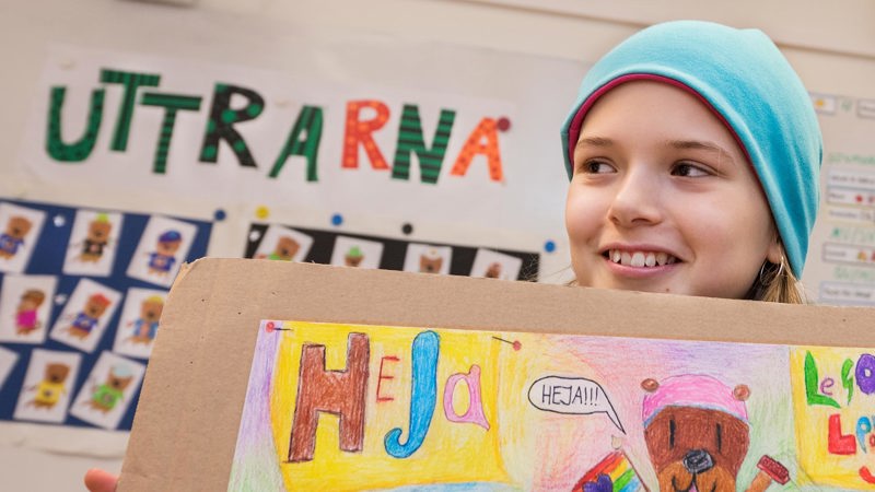 En elev håller upp en teckning med ordet heja och en seriefigur som säger heja.