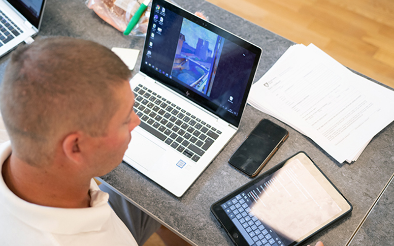 En man med papper, en dator, en mobiltelefon och en Ipad framför sig på bordet.