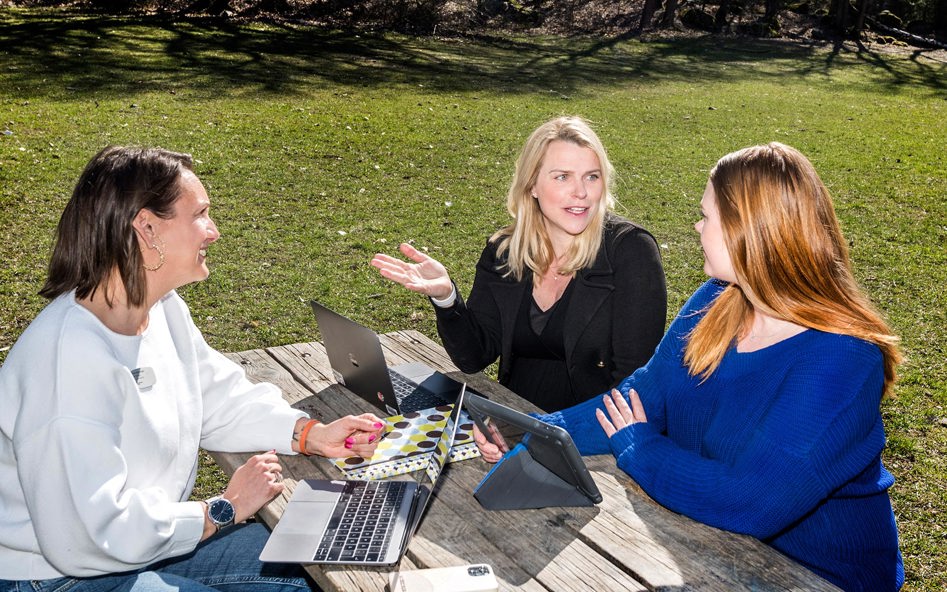 Tre lärarassistenter sitter utomhus vid ett bord och arbetar.