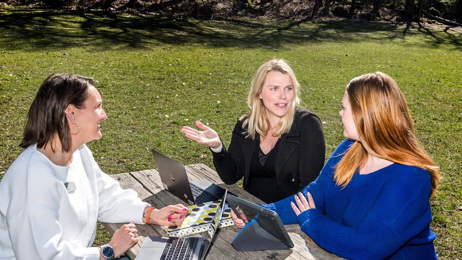 Tre lärarassistenter sitter utomhus vid ett bord och arbetar.