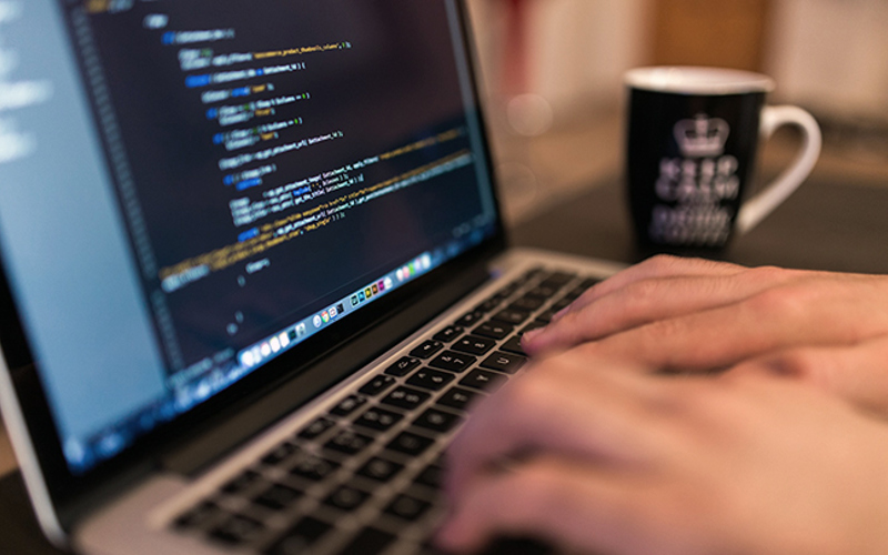 En datorskärm som visar programmeringskod och händer på ett tagngentbord.