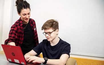 En kvinna i 40-årsåldern hjälper en högstadiekille som arbetar vid sin bärbara dator.