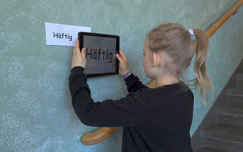 En flicka fotar en lapp på väggen med texten Häftig med sin Ipad.