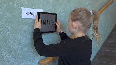 En flicka fotar en lapp på väggen med texten Häftig med sin Ipad.