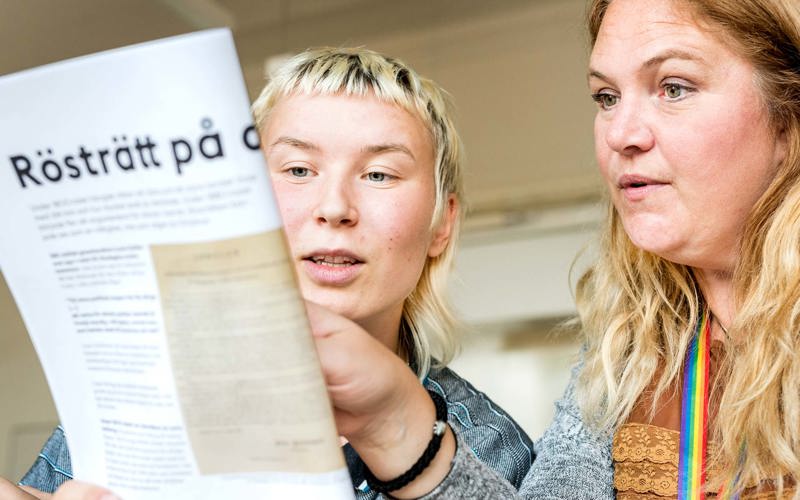 Två personer tittar på en trycksak där ordet rösträtt syns i en rubrik.