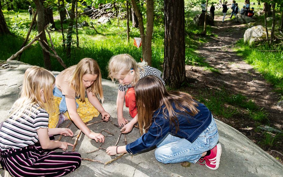På en klipphäll sitter fyra flickor och löser gemensamt ett problem som består av att flytta pinnar.