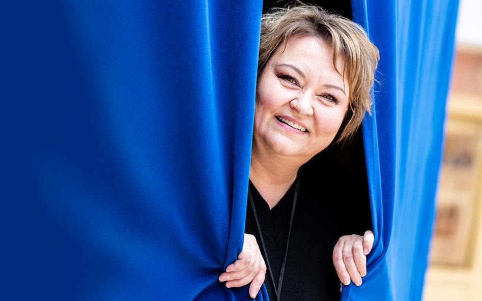 Rektor Raija Ikonen tittar ut mellan två blå draperier.