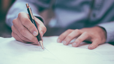 Hand som håller i en penna, skriver på papper