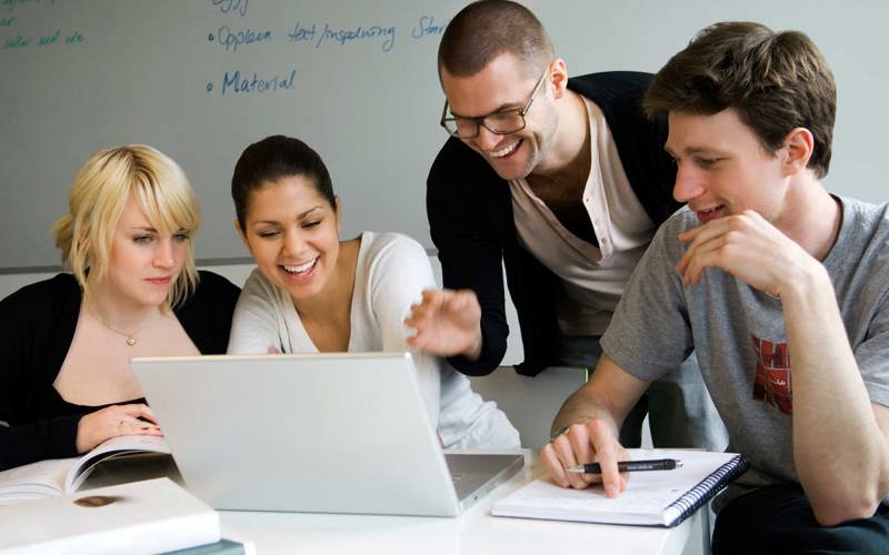 Tre glada elever och en pedagog tittar på en datorskärm.