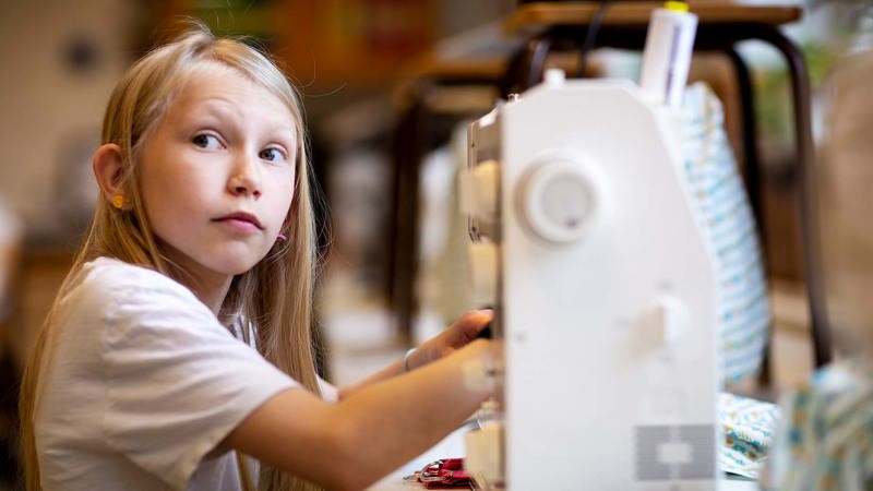 En elev tittar upp från en symaskin som hon sitter och arbetar med.