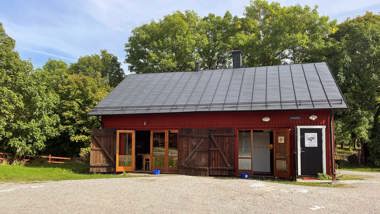 Ett rött hus med öppna dörrar och fönster med gröna träd i bakgrunden.