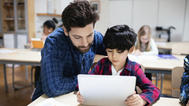 Man och pojke i ett klassrum tittar på Ipad.