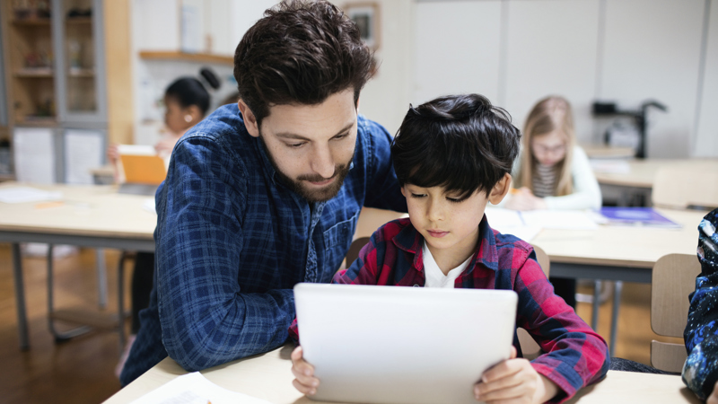 Man och pojke i ett klassrum tittar på Ipad.