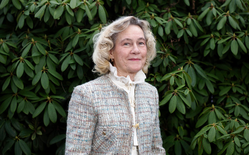 En leende Margaretha Orvarsson Hannfors står utomhus vid en stor grön rhododendronbuske.