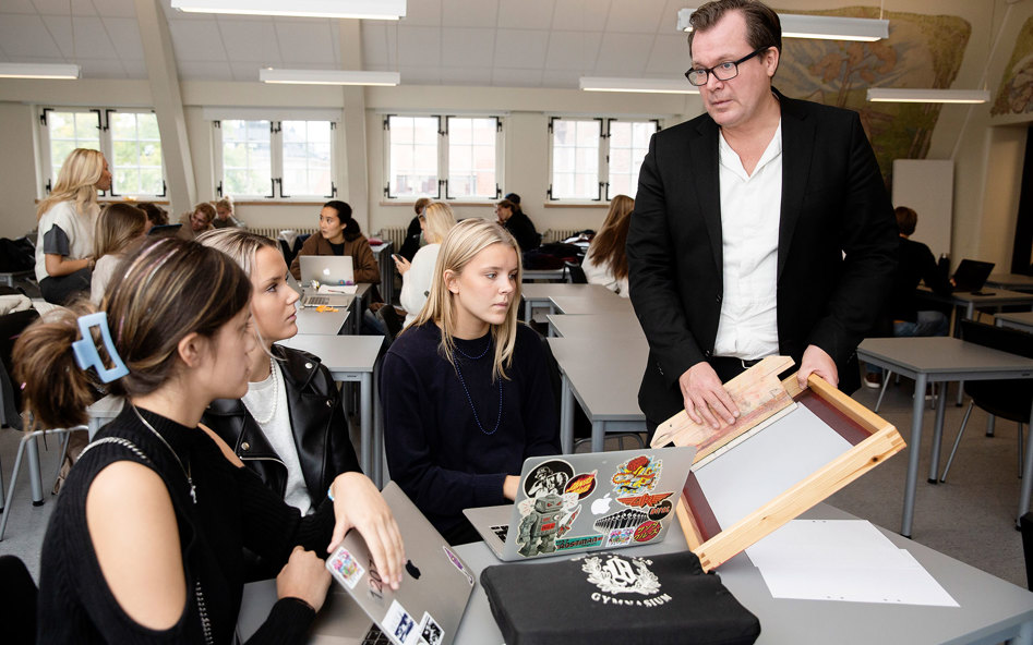 En lärare samtalar med tre elever som sitter runt ett bord i ett klassrum.