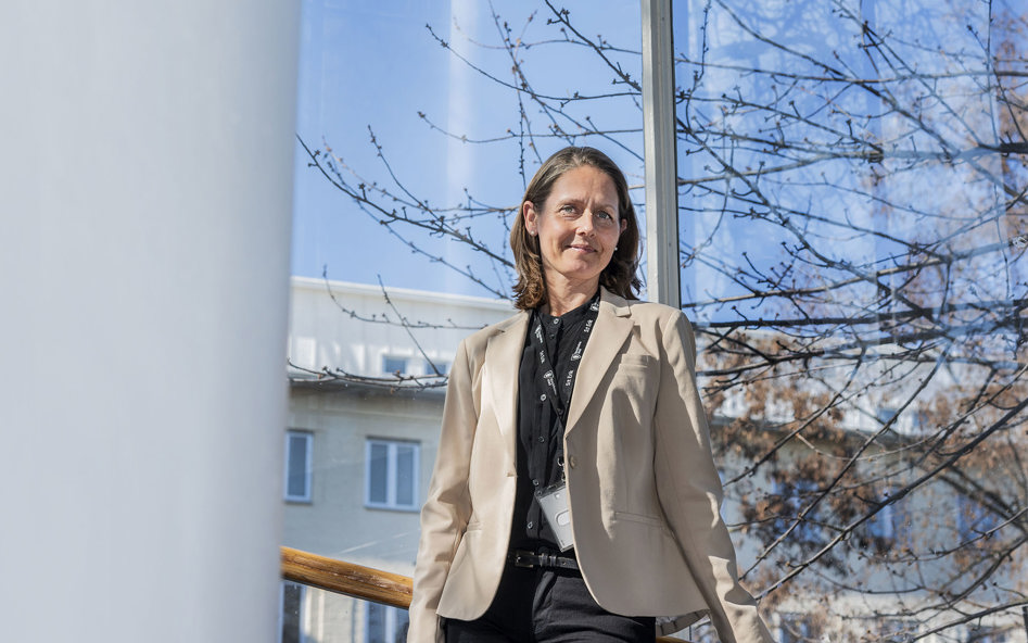 Leende kvinna framför ett fönster i en skolbyggnad.