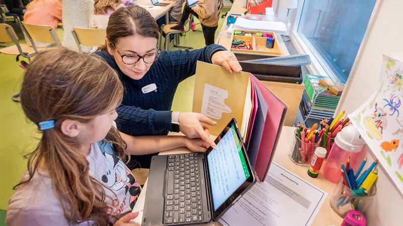 Lärare och elev studerar tillsammans med bok och laptop.