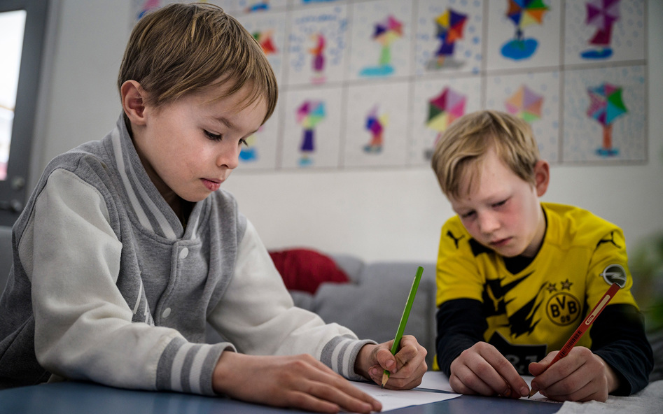 Två pojkar sitter i ett klassrum och skriver med papper och penna.